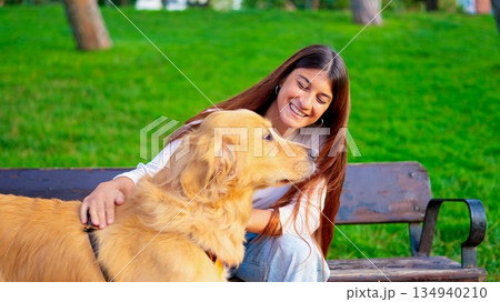 Woman petting golden retriever dog on park bench Woman petting golden retriever dog on park bench 134940210