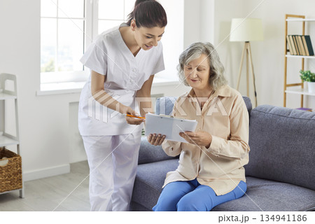 Elderly woman sitting on sofa listening to nurse, close-up Elderly woman sitting on sofa listening to nurse, close-up 134941186