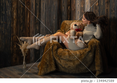 Cozy indoor scene of a woman sitting in a chair with a teddy bear during a quiet afternoon 134942589