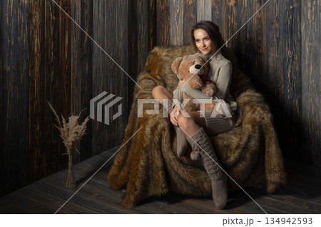 Woman sits on a fur chair holding a teddy bear in a cozy indoor setting during daylight hours Woman sits on a fur chair holding a teddy bear in a cozy indoor setting during daylight hours 134942593