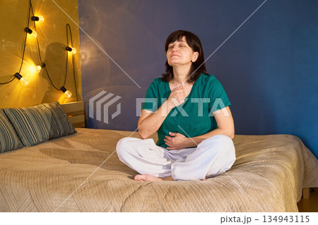 Woman focusing on her breath during meditation session on bed at home Woman focusing on her breath during meditation session on bed at home 134943115