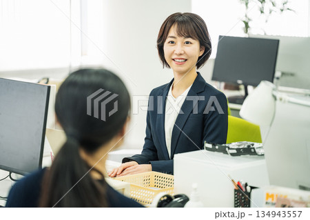 オフィスの机で同僚を話をする若い女性 134943557