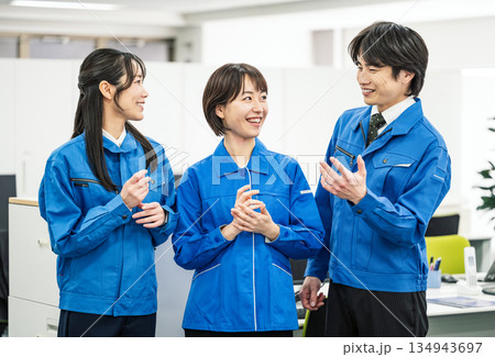 オフィスで話をする青い作業服を着た若い男女 134943697