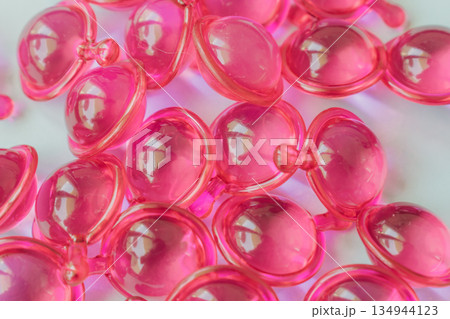 Close-up macro shot of many glossy pink hair treatment capsules. Focused foreground highlights the rich oil and reflective texture Close-up macro shot of many glossy pink hair treatment capsules. Focused foreground highlights the rich oil and reflective texture 134944123