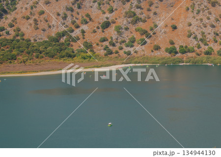 Drying mountain lake with wide strip of dried shore and orange rocky slope. 134944130