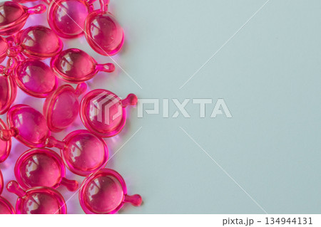 Bright pink hair capsules border on the left side of a clean light background, providing generous copy space for text, promotional cosmetic health care advertising 134944131