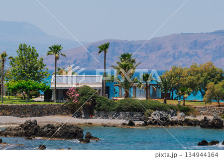 Picturesque landscape from the paradise Greek island of Crete. Cozy house by the sea surrounded by palm trees and greenery 134944164