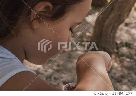 Child eating ice cream from a paper cup with an eco-friendly wooden spoon outdoors 134944177