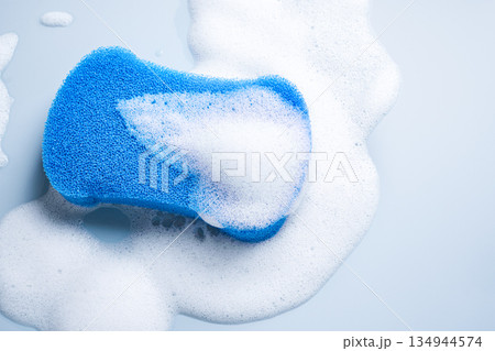 Blue sponge surrounded by white soap foam on pale blue background Blue sponge surrounded by white soap foam on pale blue background 134944574