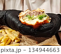 Hands in black gloves holding a juicy bitten burger. 134944663