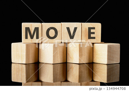 Wooden toy blocks are arranged in a stack, spelling out the word MOVE. The arrangement sits atop a reflective surface in front of a dark, seamless background 134944708