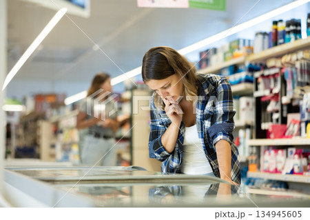 Young woman choosing frozen food in supermarket Young woman choosing frozen food in supermarket 134945605