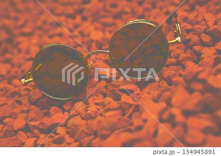 Blurred smooth vintage cool gold sunglasses on pebbles red stones Blurred smooth vintage cool gold sunglasses on pebbles red stones 134945891