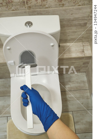 Hand wearing blue glove holding silicone toilet brush for hygiene and sanitation 134947244