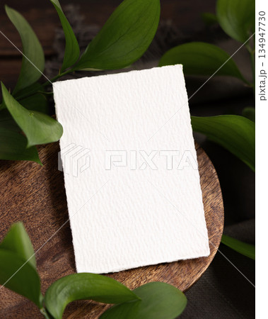 Vertical card on brown wooden tray near green leaves and grey linen cloth closeup, boho mockup Vertical card on brown wooden tray near green leaves and grey linen cloth closeup, boho mockup 134947730