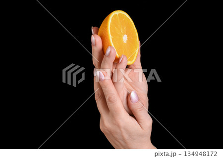A human hand holding a fresh half orange on a black background 134948172