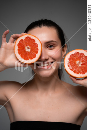 Smiling woman holding fresh grapefruit halves near face on neutral background, healthy lifestyle, natural beauty, vitamins, wellness concept Smiling woman holding fresh grapefruit halves near face on neutral background, healthy lifestyle, natural beauty, vitamins, wellness concept 134948581