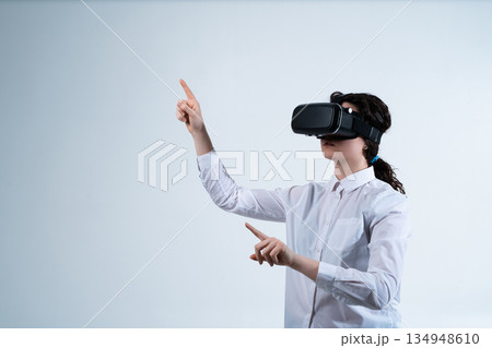 Woman using virtual reality headset and interacting with advanced digital interface through hand tracking technology on clean white studio background Woman using virtual reality headset and interacting with advanced digital interface through hand tracking technology on clean white studio background 134948610
