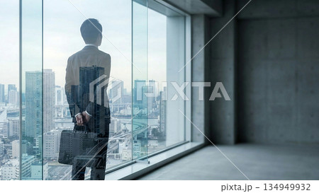朝日夕日の高層ビルの窓辺に立ち光の中で都市を眺めるビジネス人物の後ろ姿。広がる景色が前進や成長を表現 134949932