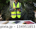 Engineer man wearing a high-visibility safety vest and a hard hat, checking operation of solar panel system with digital tablet or smartphone. 134951853