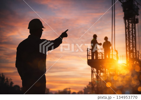 Construction Site Supervisor Pointing Direction at Sunset with Industrial Silhouettes 134953770