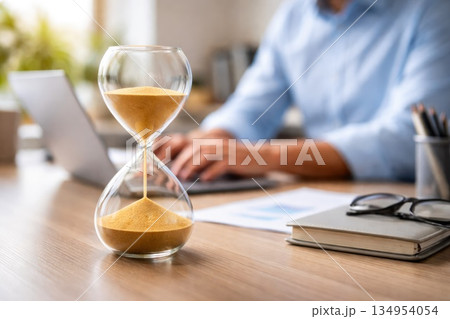 Hourglass on Office Desk Symbolizing Time Management and Productivity Hourglass on Office Desk Symbolizing Time Management and Productivity 134954054