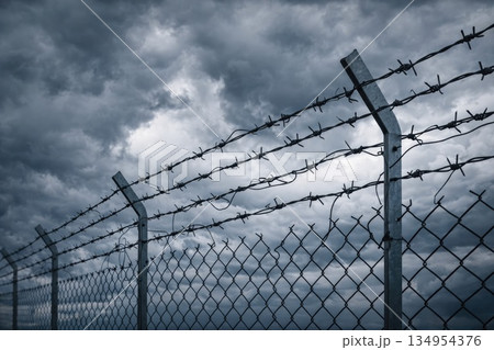 Barbed Wire Fence Under Dark Stormy Sky Representing Restriction, Danger and Security Barbed Wire Fence Under Dark Stormy Sky Representing Restriction, Danger and Security 134954376