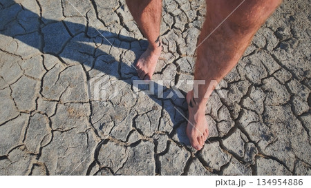 A man walks barefoot through mud and swampy cracked earth. 134954886