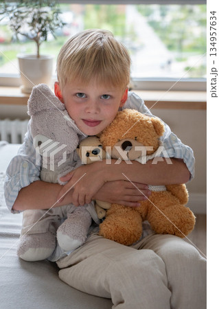 Young boy hugs soft teddy bears at home, portrait with gentle daylight, neutral colors, calm and comforting childhood moment Young boy hugs soft teddy bears at home, portrait with gentle daylight, neutral colors, calm and comforting childhood moment 134957634