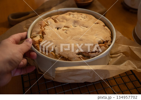 Freshly baked apple pie with golden crust cools in a baking dish on parchment paper, warm tones, cozy homemade baking atmosphere 134957702