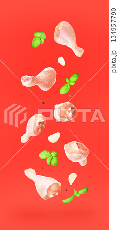 Flying raw chicken drumsticks with fresh basil, garlic and spices isolated on red background. Creative food levitation concept. High quality photo 134957790