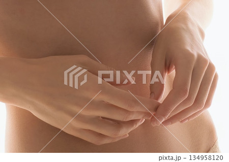 Close-up of a woman's hands gently touching her torso and stomach. 134958120