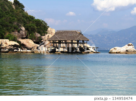 A small wooden hut is on a beach next to a body of water A small wooden hut is on a beach next to a body of water 134958474
