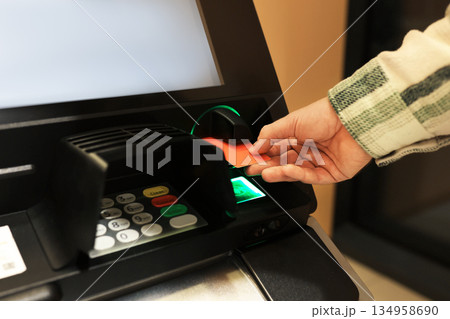 Man inserting orange credit card into ATM slot. Hand holding bank card at automated teller machine close up. High quality photo Man inserting orange credit card into ATM slot. Hand holding bank card at automated teller machine close up. High quality photo 134958690