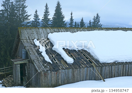 Snow lies on the roof of a wooden house. Winter in a mountain village Snow lies on the roof of a wooden house. Winter in a mountain village 134958747
