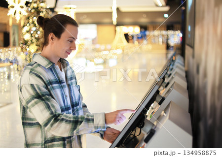 man using interactive touchscreen kioskkiosk, touchscreen, man, shopping, mall, christmas, interactive, digital, tec in shopping mall with Christmas decoration lights in background. High quality photo 134958875