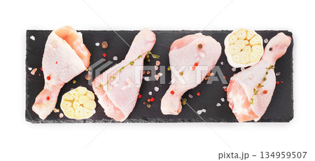 Top view of raw chicken drumsticks with garlic and spices on black slate board isolated on white background. High quality photo Top view of raw chicken drumsticks with garlic and spices on black slate board isolated on white background. High quality photo 134959507