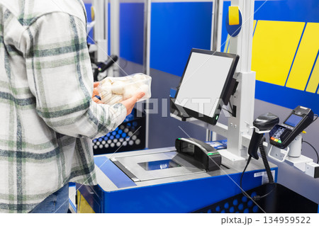 A customer holds mushrooms at a self-checkout counter in a supermarket. High quality photo 134959522
