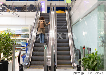 Adult caucasian woman riding escalator inside airport terminal with backpack and passport 134959574