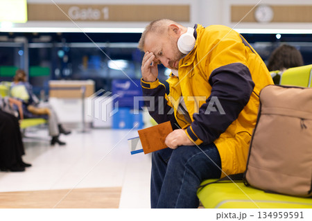 Tired adult caucasian man sitting in airport waiting area holding passport 134959591