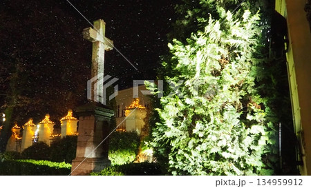 On Christmas New Year Eve, during snowstorm and blizzard, religious Orthodox cross stands firm in churchyard. A thuja tree, covered in snow, sways in the winter wind. A symbol of faith and fortitude. On Christmas New Year Eve, during snowstorm and blizzard, religious Orthodox cross stands firm in churchyard. A thuja tree, covered in snow, sways in the winter wind. A symbol of faith and fortitude. 134959912