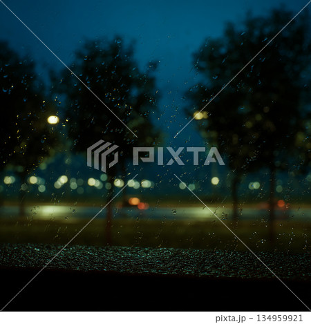 photo depicting rainy evening scenery, in the foreground raindrops, in the background blurred silhouettes of trees and lanterns 134959921