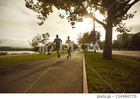 Two runners training on tree lined park path at sunrise, urban cardio workout 134960770