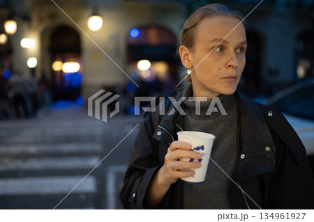 Woman holding coffee cup on evening street Woman holding coffee cup on evening street 134961927