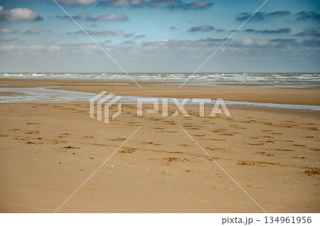 A wide view of Omaha Beach's peaceful shoreline in Normandy, France. Once a historic World War II landing site, the beach now offers a calm and reflective coastal landscape. A wide view of Omaha Beach's peaceful shoreline in Normandy, France. Once a historic World War II landing site, the beach now offers a calm and reflective coastal landscape. 134961956
