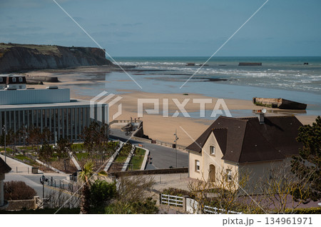 A wide scenic view of Arromanches-les-Bains, France, showcasing the town and its historic beach. This D-Day landing site is now a peaceful coastal destination rich with World War II history. A wide scenic view of Arromanches-les-Bains, France, showcasing the town and its historic beach. This D-Day landing site is now a peaceful coastal destination rich with World War II history. 134961971