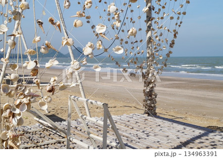 Strings of white seashells hang in clusters against a backdrop of turquoise sea, blue sky and golden sand. 134963391