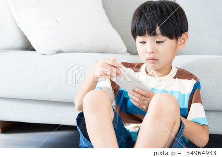 リビングでスマホで遊ぶ小学生男子 リビングでスマホで遊ぶ小学生男子 134964933