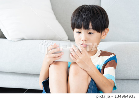 リビングでスマホで遊ぶ小学生男子 リビングでスマホで遊ぶ小学生男子 134964935