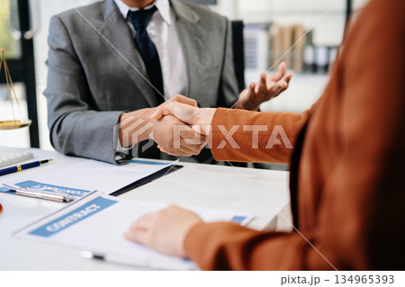 Woman lawyer hand and women client shaking hand collaborate on working agreements with contract documents at the office. Woman lawyer hand and women client shaking hand collaborate on working agreements with contract documents at the office. 134965393